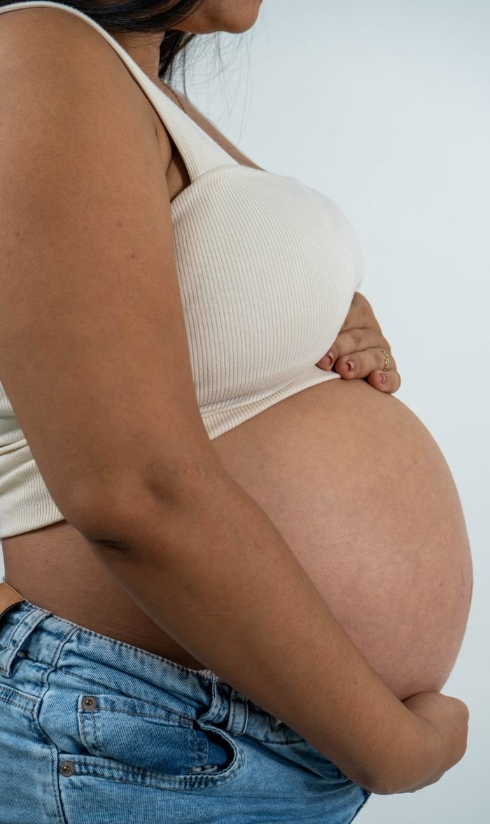 Side view of a pregnant woman in casual clothing holding her belly, symbolizing motherhood and anticipation.